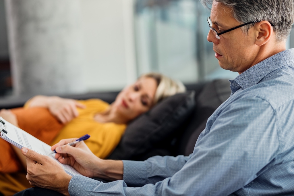 Male psychiatrist writing notes while having counseling with a patient at his office.