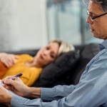 Male psychiatrist writing notes while having counseling with a patient at his office.