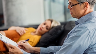 Male psychiatrist writing notes while having counseling with a patient at his office.